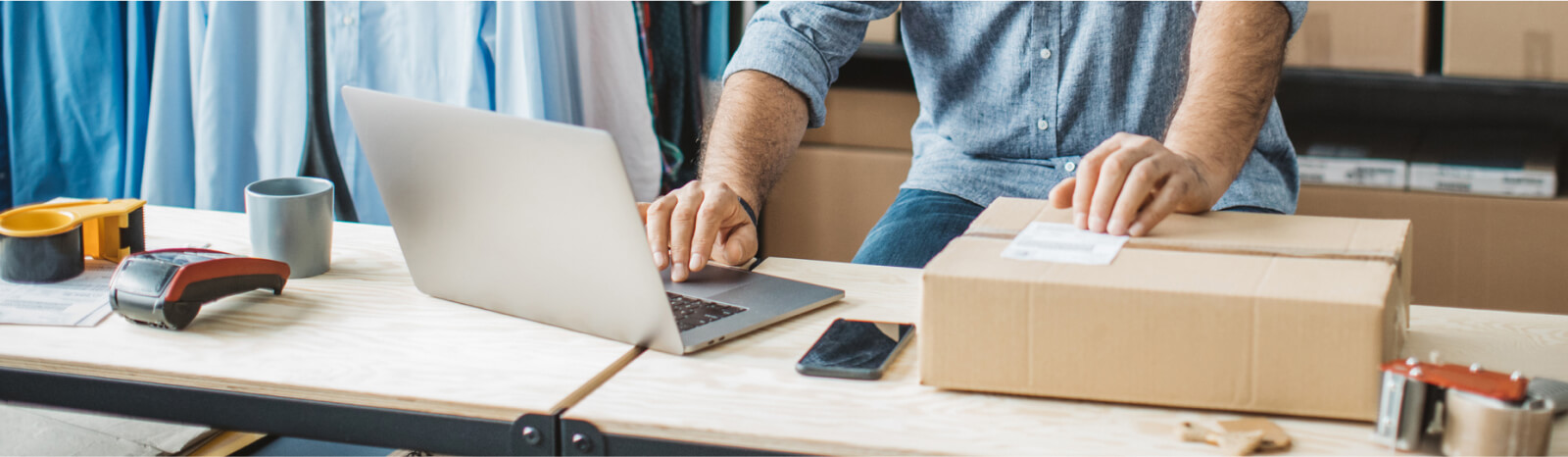 A man's hands resting on a shipping box and the keyboard of a laptop.