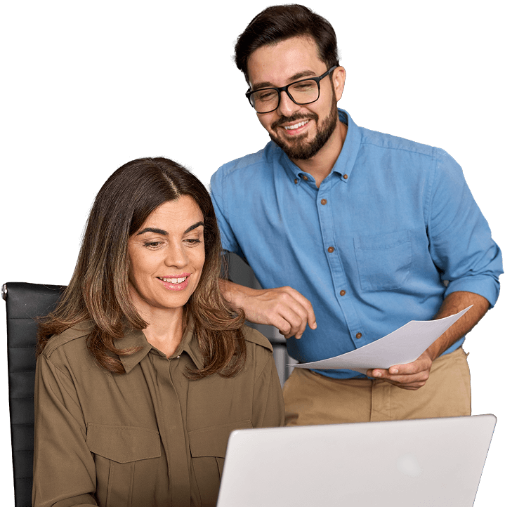 woman sitting in a chair and man holding papers both looking at a computer screen